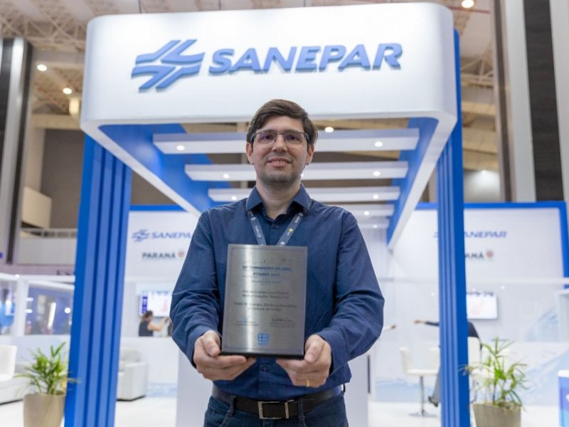 Homem com placa de reconhecimento nas mãos em frente a um estande com a logo da Saneapar.