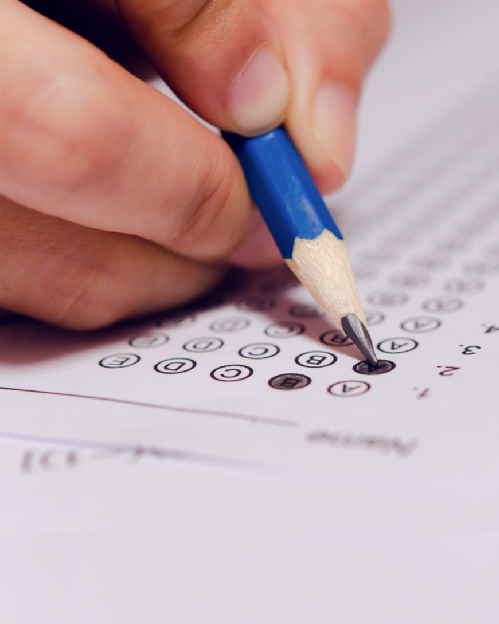 Mão segurando um lápis azul fazendo anotação em um gabarito de papel