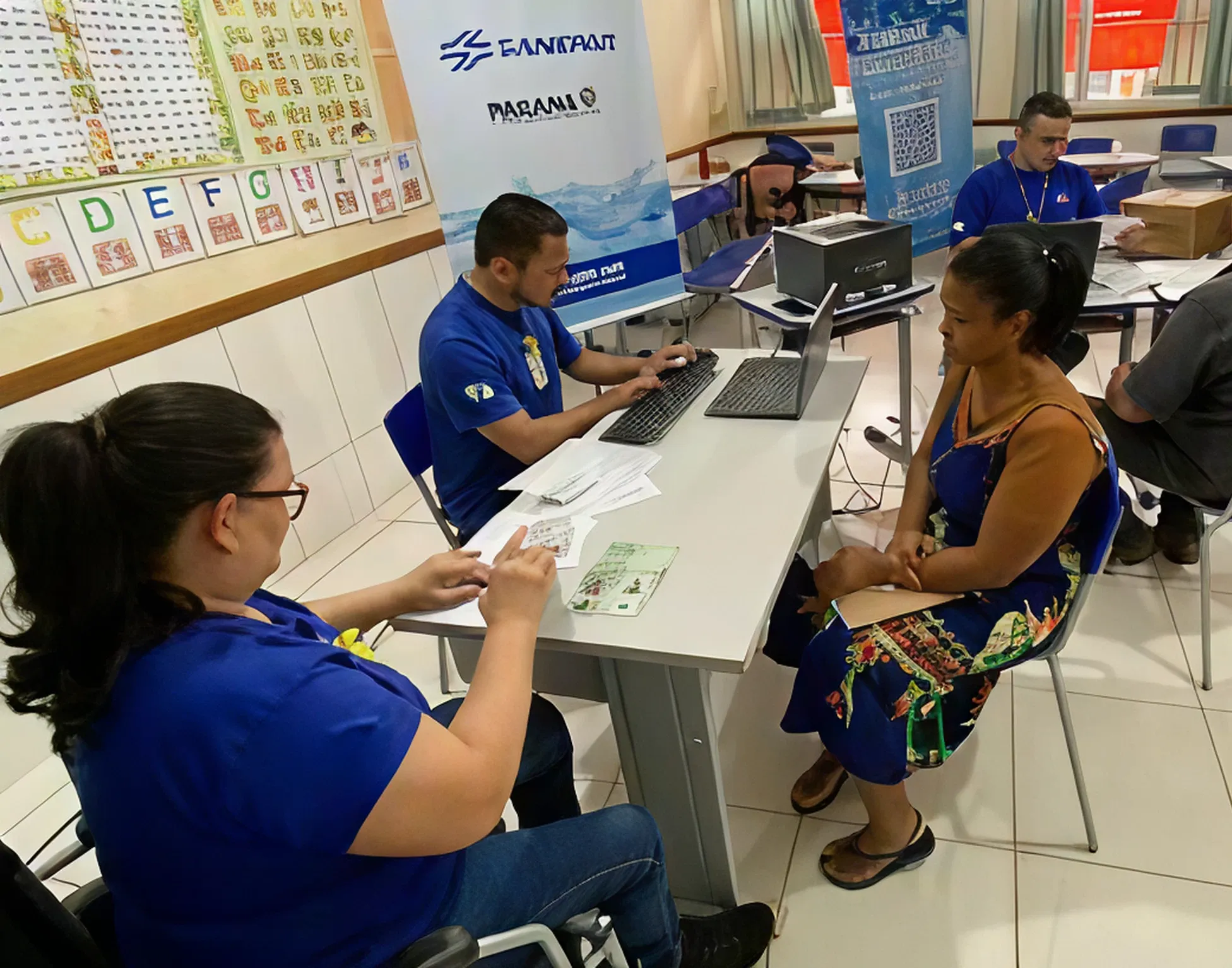 Sala de atendimento comercial da Sanepar com cinco atendentes sentados, mexendo em computadores e atendendo clientes.