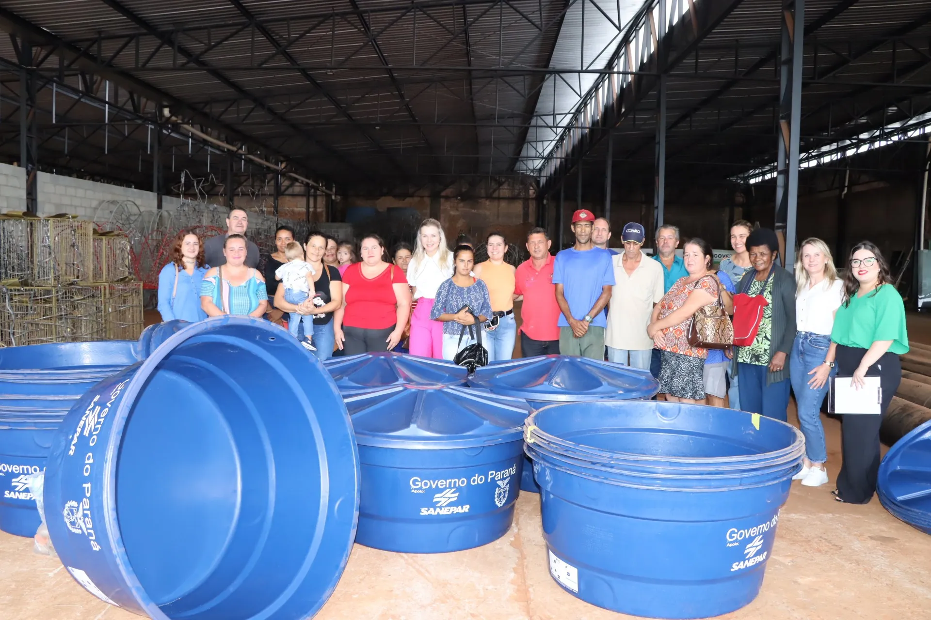 Grupo de pessoas em um galpão coberto atrás de diversas caixas d'água azuis