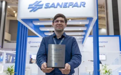 Homem com placa de reconhecimento nas mãos em frente a um estande com a logo da Saneapar.