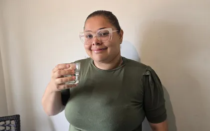 mulher sorri com copo de água na mão