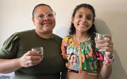 mãe e filha sorriem com copo de água na mão