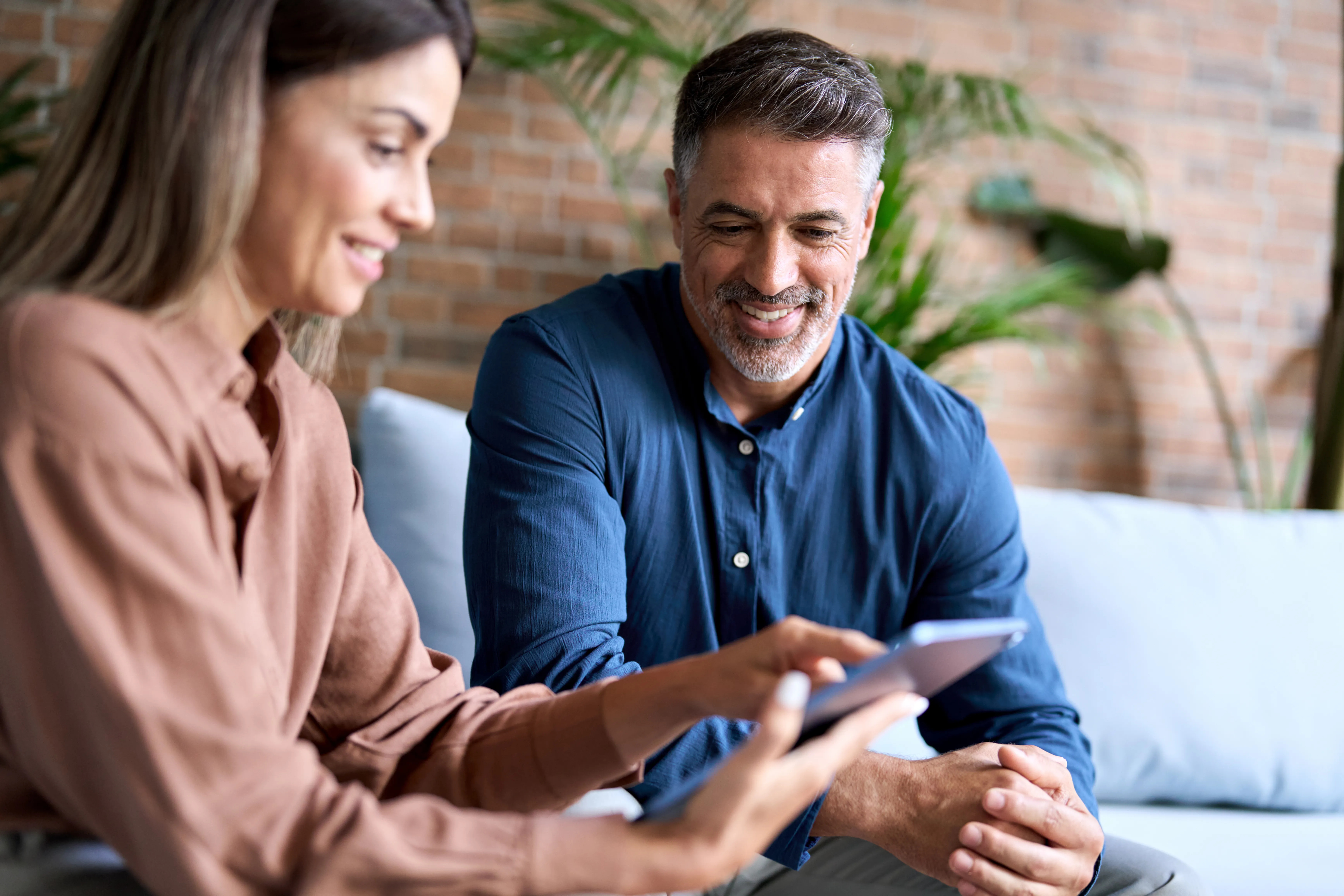 Casal de um homem e uma mulher conversando sorrindo sentados em um sofá dentre de casa