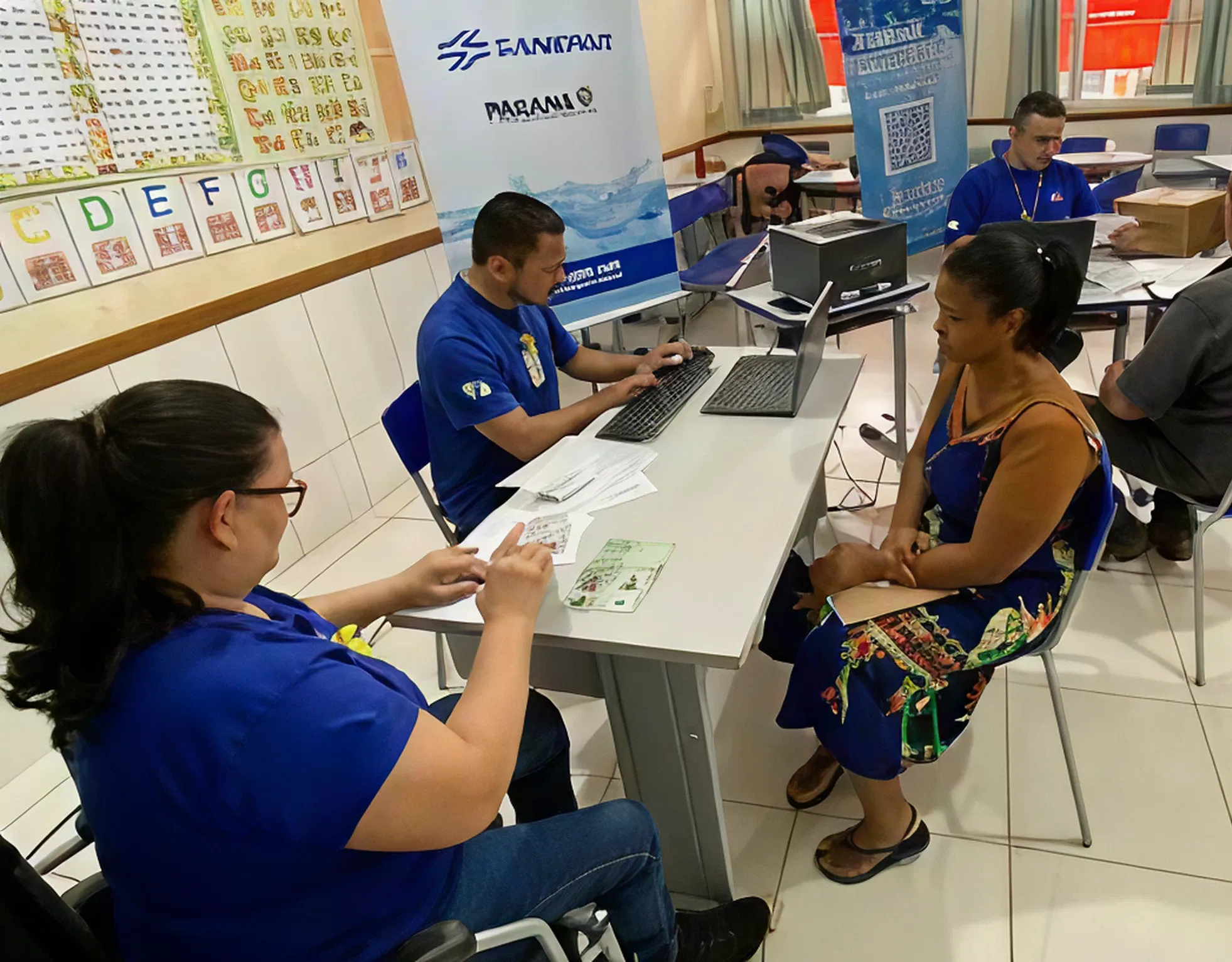 Sala de atendimento comercial da Sanepar com cinco atendentes sentados, mexendo em computadores e atendendo clientes.